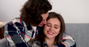 Oturma odasında kanepede oturmuş öpüşen genç bir çift.