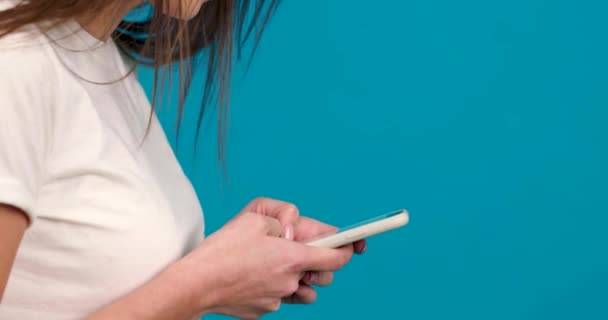 Vista lateral de chica alegre usando smartphone con sonrisa aislada sobre fondo azul — Vídeos de Stock