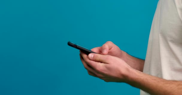 Vista cortada do homem rolagem alimentar no smartphone isolado no fundo azul — Vídeo de Stock