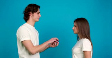 Yüzüğü olan bir adamın sürpriz kız arkadaşına evlenme teklif etmesi, öpüşmesi ve mavi arka planda izole bir şekilde kucaklaşması.