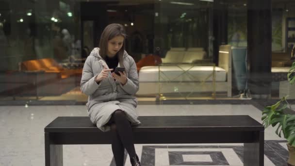 Girl scrolling on smartphone while sitting on bench and talking to boyfriend — Stock Video