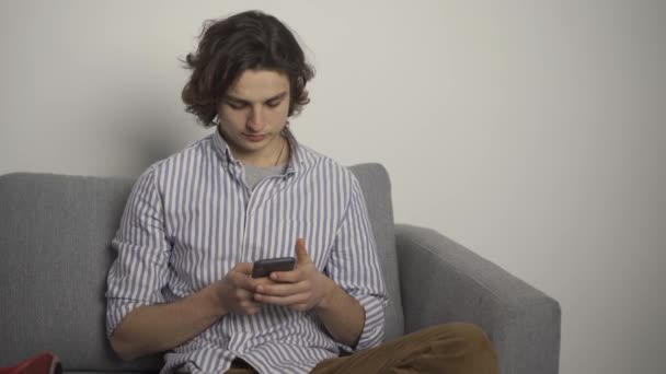 Fiatal férfi gépel okostelefonon, és mosolyogva néz a kamerába — Stock videók