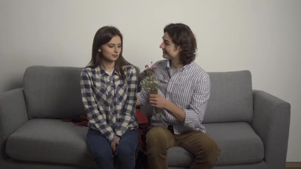 Улыбающийся мужчина закрывает глаза рукой к девушке и представляет букет в гостиной — стоковое видео