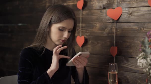 Дівчина зі склянкою шампанського посміхається і друкує на смартфоні — стокове відео
