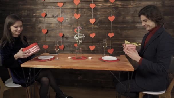 Pareja feliz intercambiando regalos de San Valentín y mirándose con sonrisa — Vídeos de Stock