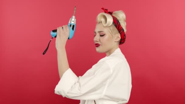 Smiling blonde pin up girl holding drill on pink background — Stockvideo