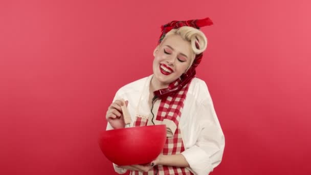 Smiling pin up girl cooking and talking on telephone on pink background — Stock Video