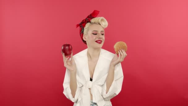 Sonriendo pin up chica sosteniendo manzana y hamburguesa — Vídeo de stock