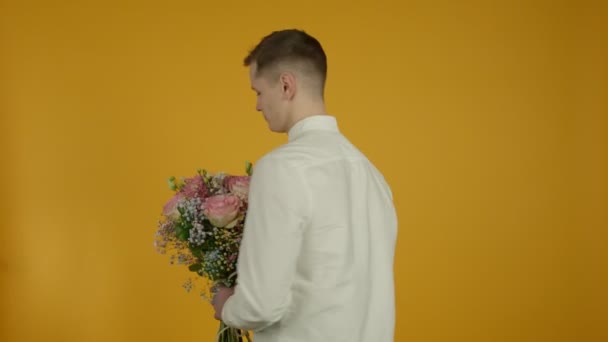 Cheerful young man in white shirt showing flowers — Stockvideo