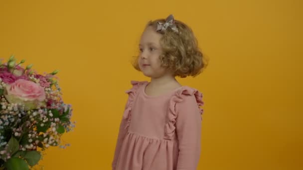 Lindo niño rizado sosteniendo flores y mirando a la cámara — Vídeos de Stock