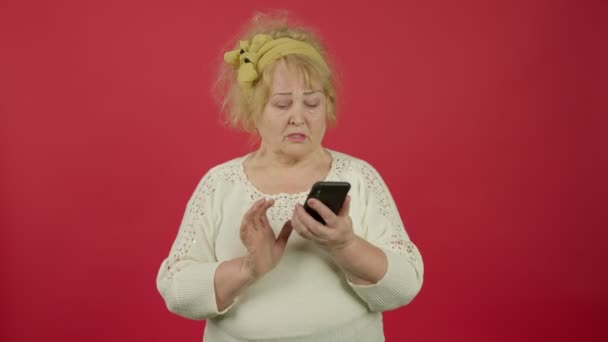 실망 한 나이든 체중 과다인 여성 이 스마트폰으로 타이핑을 하고 빨간 배경으로 전화를 걸었습니다 — 비디오
