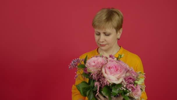 Зріла жінка тримає букет еустоми і нюхає квіти з посмішкою — стокове відео