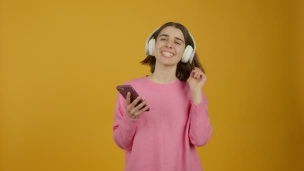 ヘッドフォンで音楽を聞き、笑顔で踊るスマートフォンを持つ女の子 — ストック動画