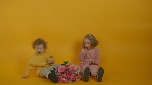 Underbara barn med blommor som ler och tittar på varandra medan de äter godis — Stockvideo