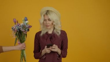 Şapkalı çekici sarışın kız akıllı telefonda yazı yazıyor ve lale buketini reddediyor.