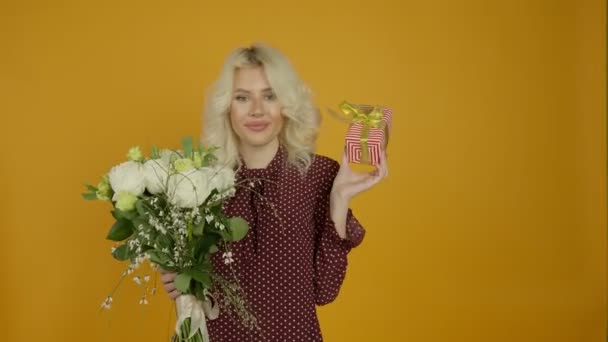 Chica sonriente sosteniendo flores y adivinando lo que en caja de regalo — Vídeo de stock