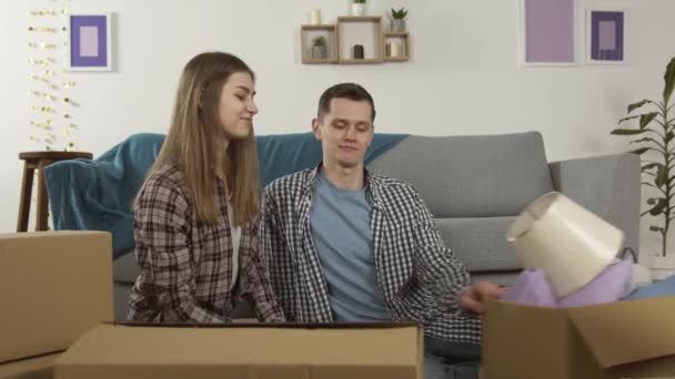 Улыбающаяся пара распаковывает коробки и обнимается в гостиной — стоковое видео