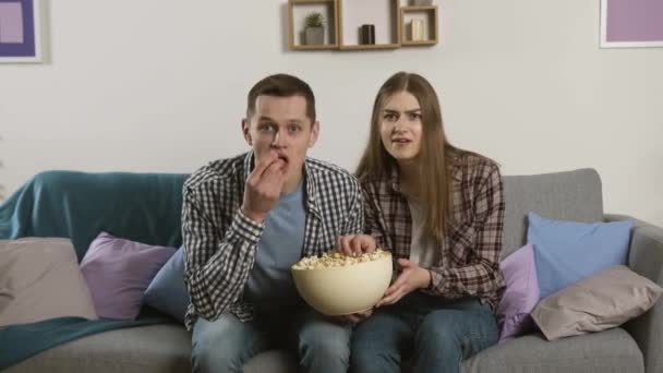 Oroade par sitter på soffan och kastar popcorn till kameran — Stockvideo