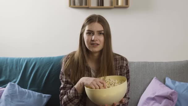 Bezorgd meisje met popcorn kijken film op de bank — Stockvideo