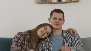 Mutlu çift kanepede kucaklaşırken ve televizyon izlerken gülüyor.
