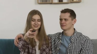 Kanepede televizyon izlerken gülümseyen bir adam kız arkadaşına göz kapatıyordu.