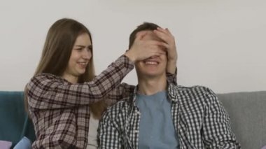 Gülen kız erkek arkadaşa gözlerini kapatıyor ve televizyon seyrediyor.