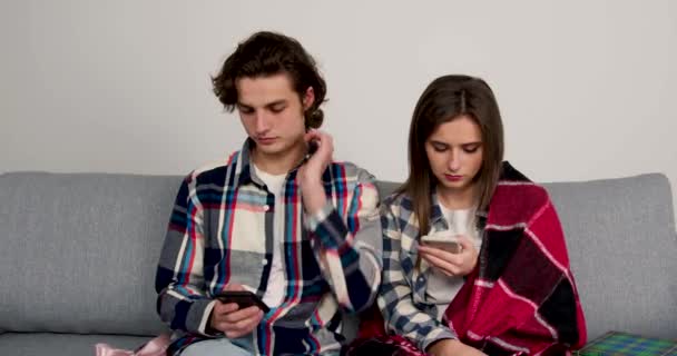 Geschäftiges Paar sitzt auf Sofa, benutzt Smartphones und tauscht Geschenke aus — Stockvideo