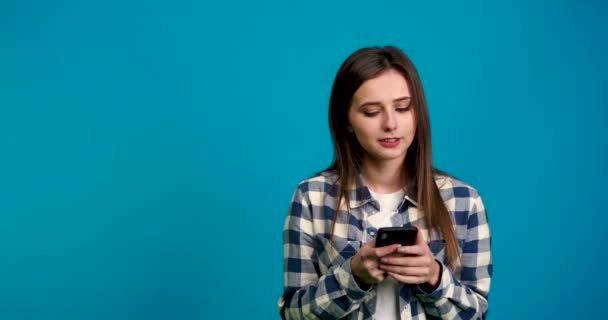 Chica mirando hacia otro lado y escribiendo en el teléfono inteligente con sonrisa — Vídeo de stock