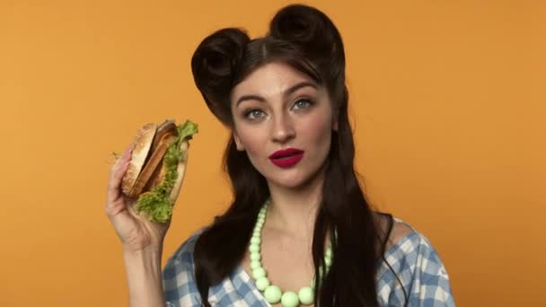 Atractivo pin up mujer sosteniendo hamburguesa con queso y mirando a la cámara — Vídeos de Stock