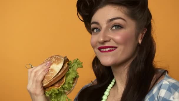 Счастливая женщина ест бургер на желтом фоне — стоковое видео