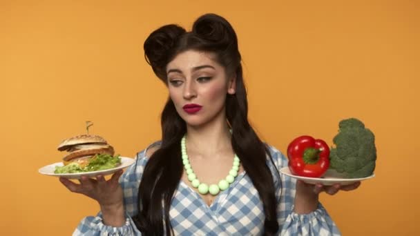 Запутавшаяся женщина не может выбрать между бургером и овощами — стоковое видео