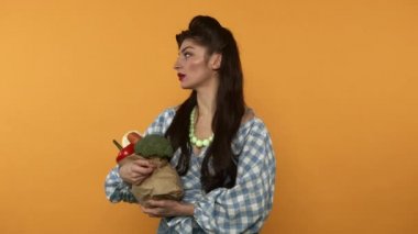 Tedirgin kadın elinde sebzelerle, kese kağıdını fırlatıp gidiyor.