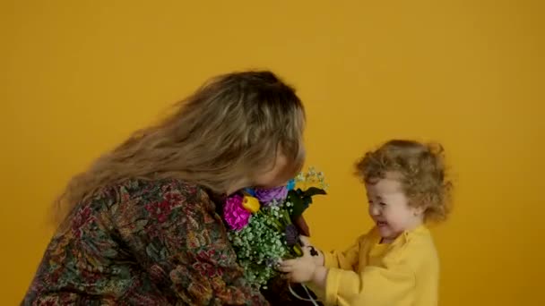 Mulher choro reconfortante criança com flores no fundo amarelo — Vídeo de Stock