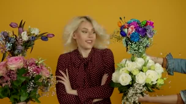 Fille blonde debout avec les bras croisés, regardant des bouquets avec un sourire surpris et renifler des fleurs — Video