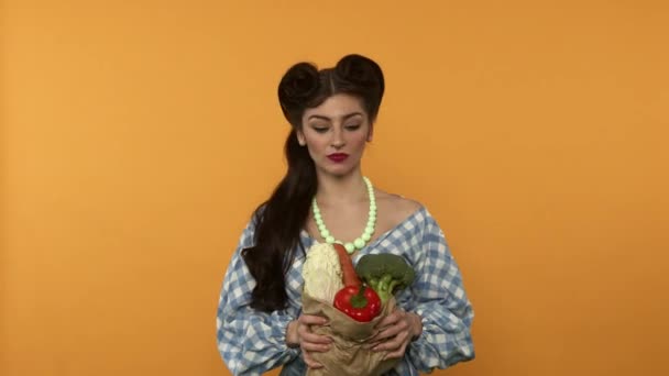 Irritée pin up femme tenant sac en papier avec des légumes après les achats sur fond jaune — Video