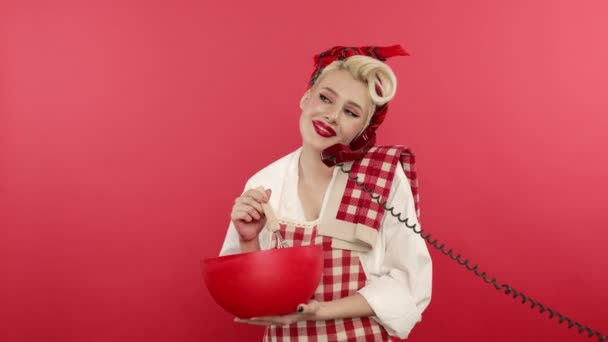 Laughing pin up girl cooking and talking on telephone on pink background — Stock Video