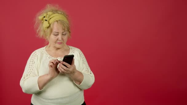 Oudere vrouw met overgewicht die wegkijkt en glimlacht terwijl ze een smartphone gebruikt — Stockvideo