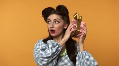 Meraklı kız hediye kutusunu kurdeleyle tutuyor ve kameraya gülümsüyor.