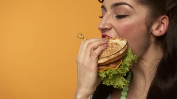 Alegre pin up mujer comiendo hamburguesa y guiñando el ojo a la cámara — Vídeo de stock