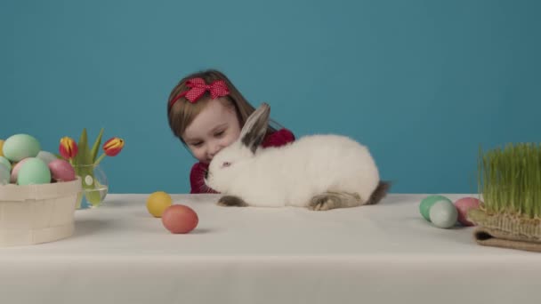 La niña feliz juega con un conejo. Le da un huevo de color de Pascua a un conejo. Feliz Pascua — Vídeo de stock