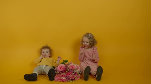 Lindos niños rizados con flores sonriendo y comiendo piruletas — Vídeo de stock