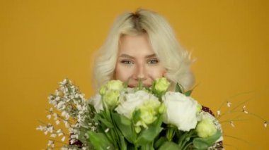 Gülümseyerek çiçekleri koklayan neşeli sarışın kızın ön görüntüsü