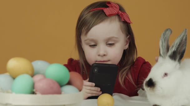 La ragazza guarda il cartone animato e accarezzando un coniglio. Il tema della Pasqua. Vacanze — Video Stock