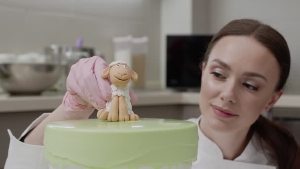 The final touch in decorating the cake, the confectioner carefully puts on the glazed surface of the sugar lamb — Stock Video
