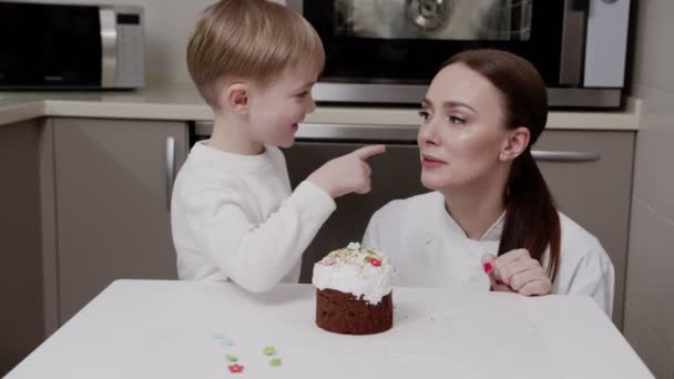Пасхальный торт, веселый досуг украшают сын и мать, они учатся и играют в одно и то же время, улыбаясь, радуясь, глядя в глаза — стоковое видео