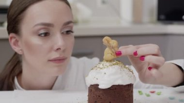 Profesyonel bir mutfakta beyaz bir tunik giyen, paskalya pastasını süsleyen, tavşan şeklinde en iyi kurabiyeleri takan, gülümseyen bir kadın.