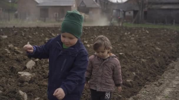 Zwei Jungen gehen spazieren, während der Traktor das Land für die Pflanzung der Erde bestellt. Gemüseanbau für Lebensmittel — Stockvideo