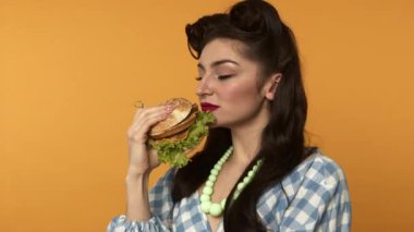 Burger koklayan, gülen ve sarı arka planda yemek yiyen bir kadın.