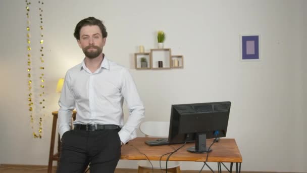 Um homem sério e confiante em um terno fica perto da área de trabalho e sorri — Vídeo de Stock