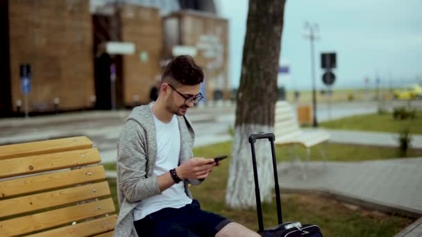 Молодий мандрівник в аеропорту, використовуючи смартфон в руках і посмішку — стокове відео